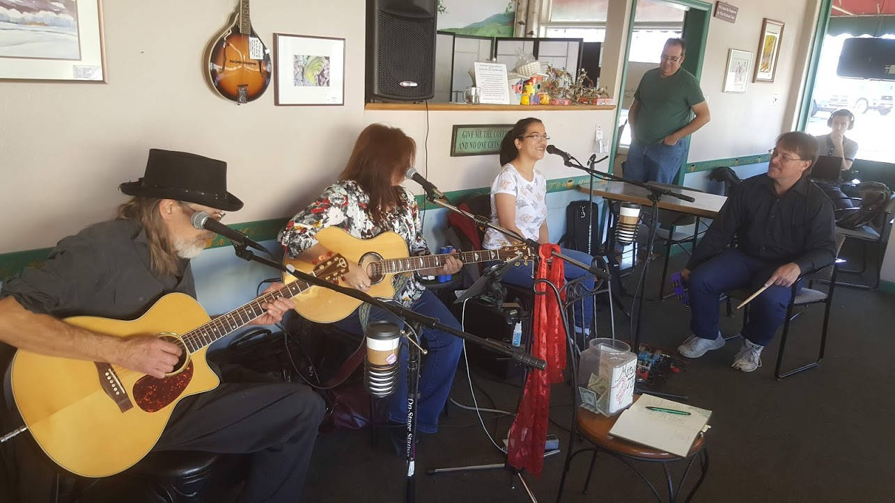 Jason's first mandolin hanging on the wall at La Dolce Vita coffee shop in Olde Town Arvada, Colorado.  In front of the mandolin are a group of musicians performing - the band, Band On The Fence, performs with guest singer Sofia Raines